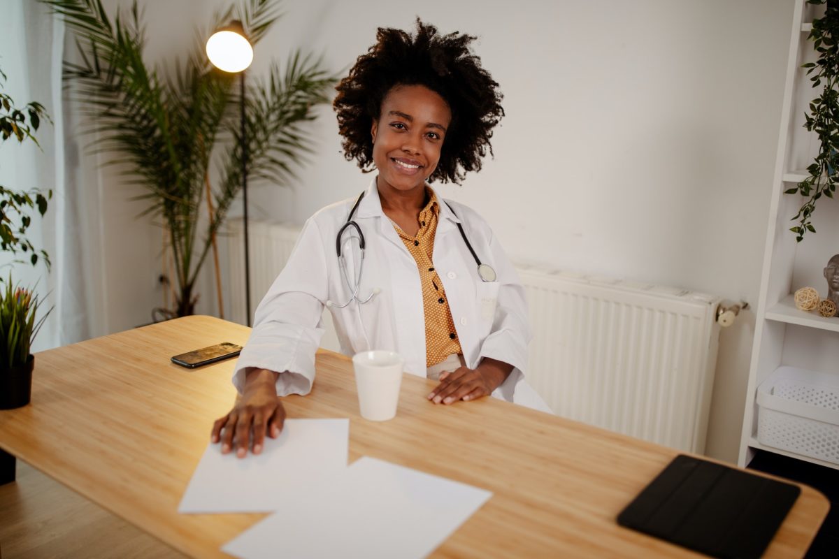 Female doctor sitting at office desk and smiling at camera, health care and prevention concept.