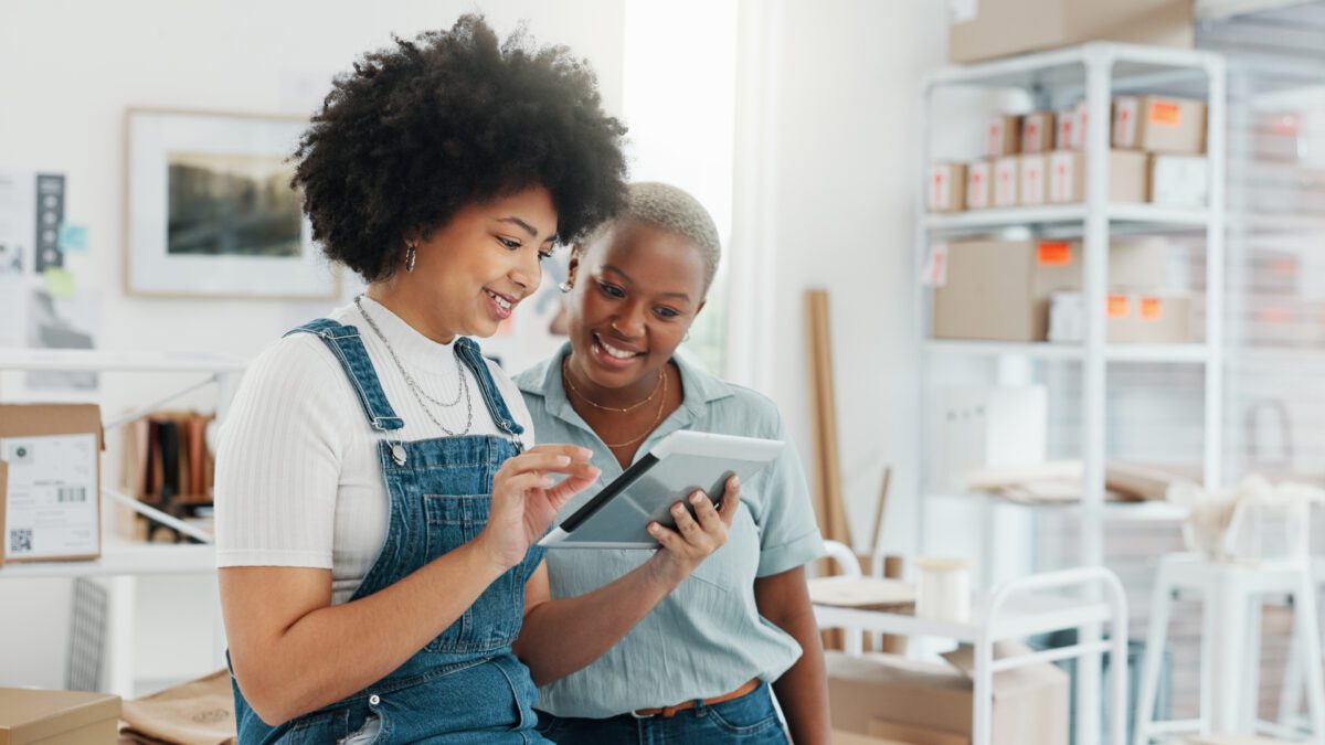 Two women smiling while looking at a tablet, exploring resources in a well-organized space