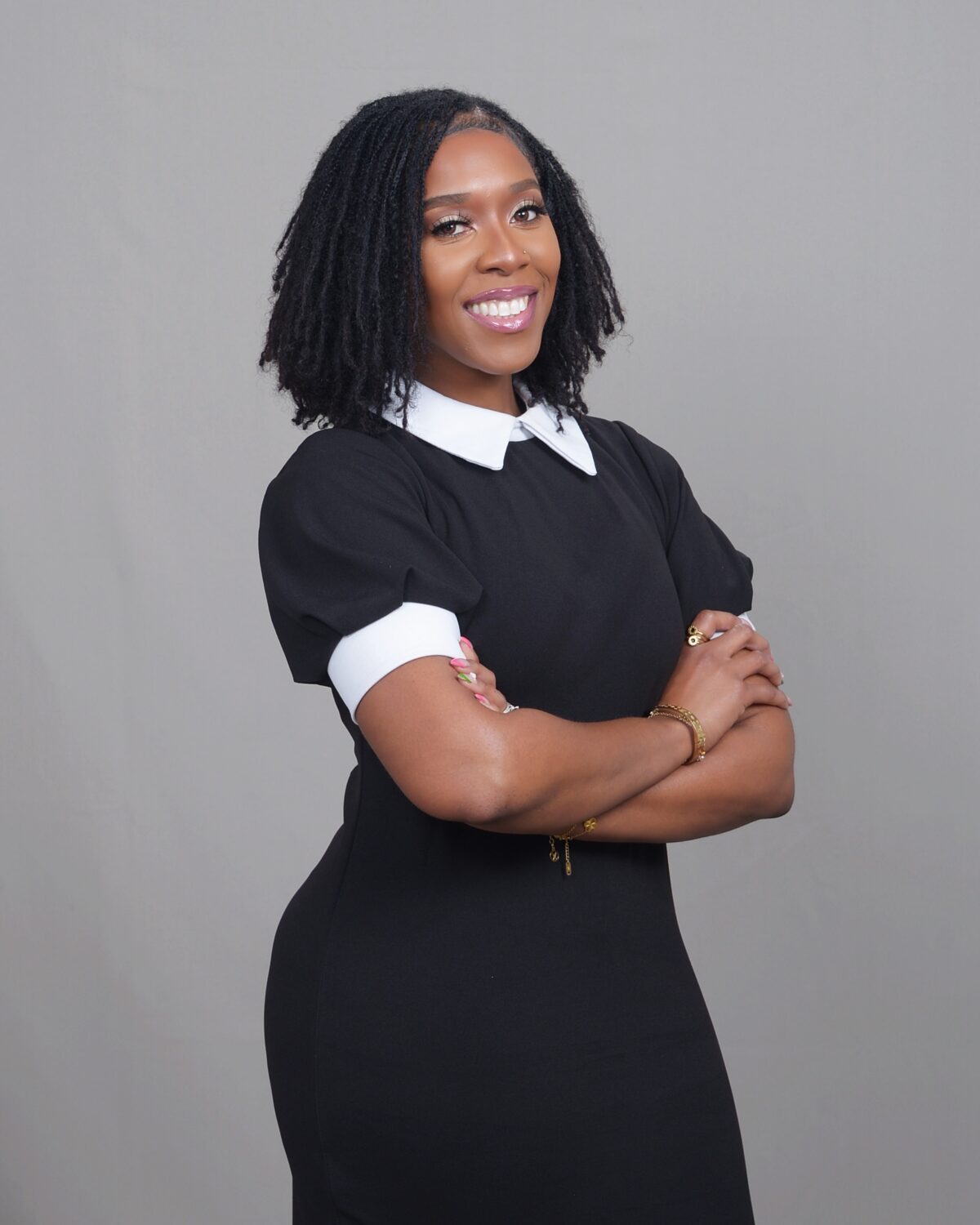 Anita Taylor posing confidently, hands on her hips, with a bright smile, in a black dress with a white collar.